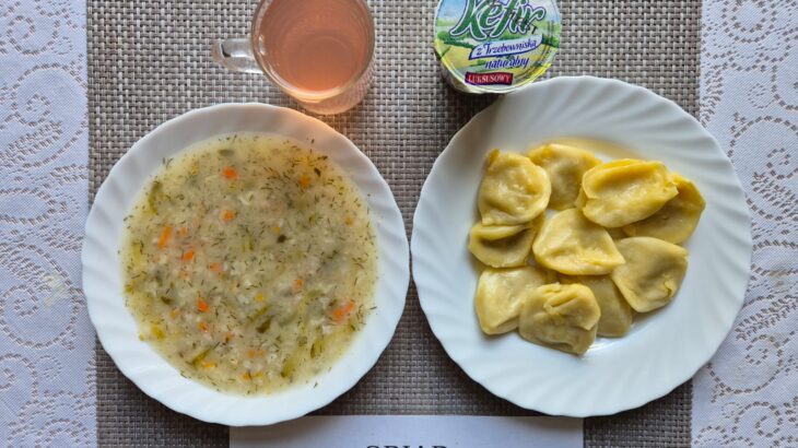 Na zdjęciu znajduję się posiłek w którego skład wchodzi Zupa ogórkowa z ryżem, Pierogi 10 szt., kefir oraz kompot z jabłek