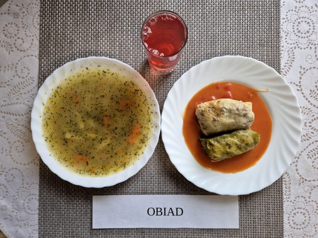 Na zdjęciu znajduję się posiłek w którego skład wchodzi Zupa ziemniaczana z czosnkiem, Gołąbki w sosie pomidorowym oraz Kompot z jabłek