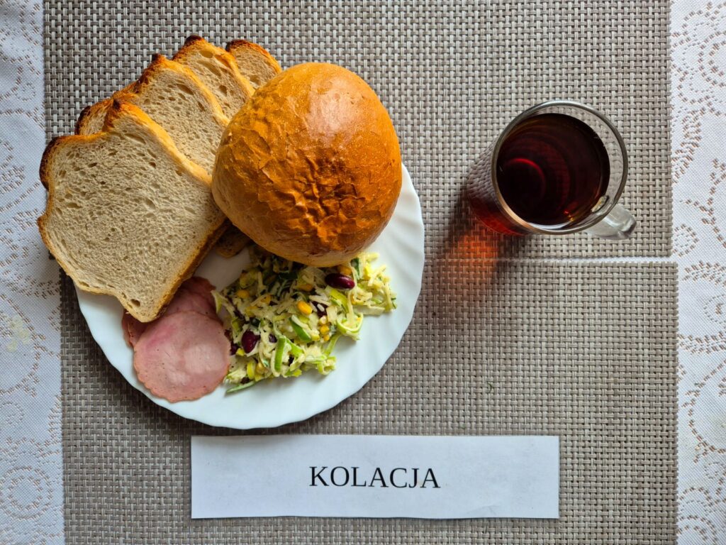 Na zdjęciu znajduję się posiłek w którego skład wchodzi Chleb pszenny, Margaryna śniadaniowa, Sałatka z pora, ananasa, i czerwonej fasoli, Bułka pszenna, wędlina drobiowa oraz Herbata czarna