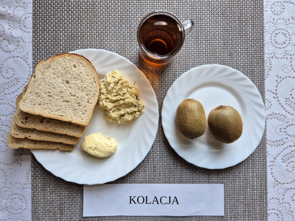 Na zdjęciu znajduję się posiłek w którego skład wchodzi Chleb pszenny, Margaryna Śniadaniowa, Pasta jajeczna, kiwi oraz Herbata czarna