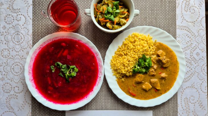 Na zdjęciu znajduję się posiłek w którego skład wchodzi Barszcz ukraiński z ziemniakami, Kasza bulgur, Gulasz wieprzowy, Surówka z ogórka kiszonego oraz Kompot z jabłek