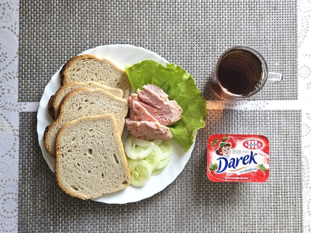 Zdjęcie przedstawia kolacje. Na zdjęciu kromki chleba, sałata, ogórki, herbata i deser