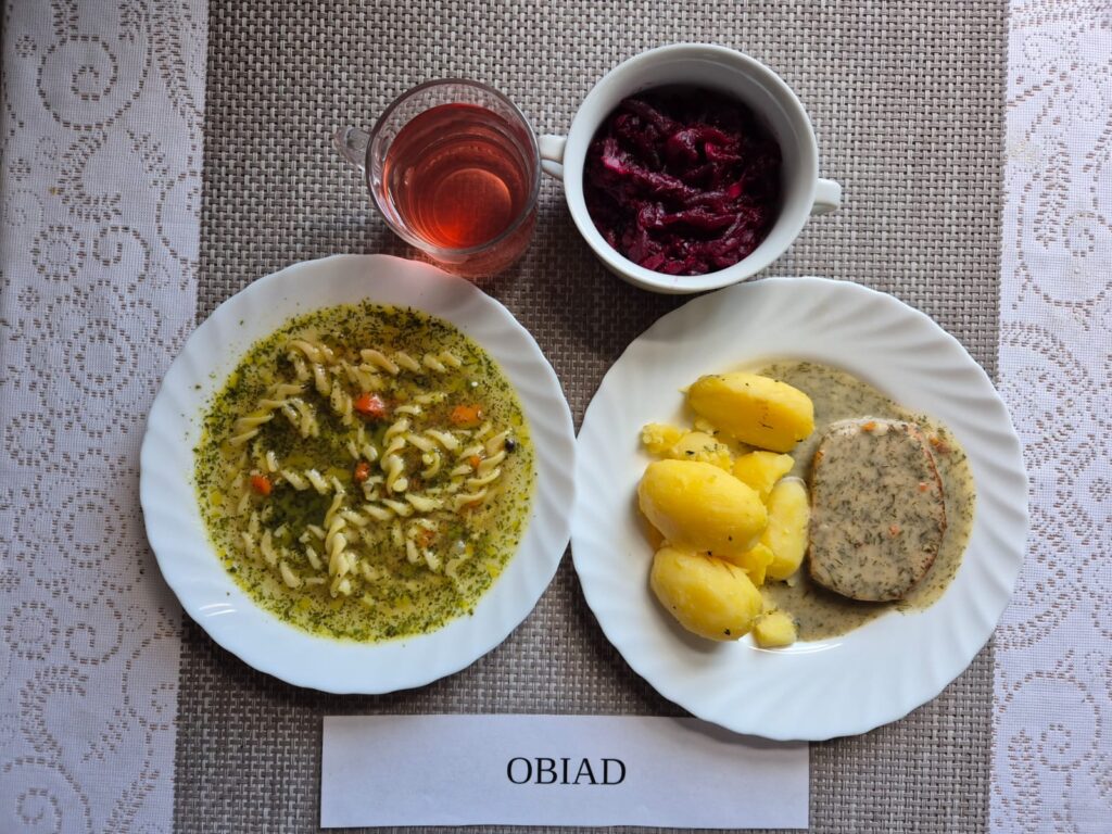 Na zdjęciu znajduję się posiłek w którego skład wchodzi Zupa jarzynowa z makaronem, Pieczeń rzymska w sosie koperkowym, Ziemniaki, Surówka z buraka, Kompot z jabłek