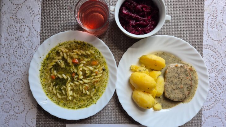 Na zdjęciu znajduję się posiłek w którego skład wchodzi Zupa jarzynowa z makaronem, Pieczeń rzymska w sosie koperkowym, Ziemniaki, Surówka z buraka, Kompot z jabłek