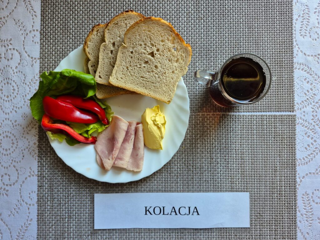 Na zdjęciu znajduję się posiłek w którego skład wchodzi Chleb pszenny, Margaryna Śniadaniowa, Kiełbasa krakowska drobiowa, Sałata masłowa, Papryka, Herbata czarna