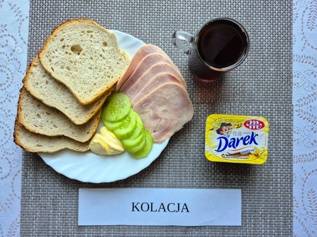 Na zdjęciu znajduję się posiłek w którego skład wchodzi Chleb pszenny, margaryna śniadaniowa, Konserwa mięsna, ogórek zielony, Rukola oraz Herbata czarna