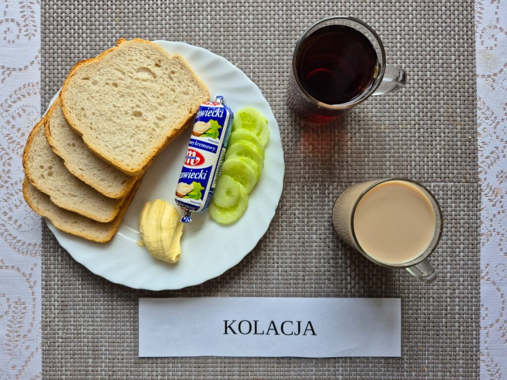 Na zdjęciu znajduję się posiłek w którego skład wchodzi Chleb pszenny, Margaryna Śniadaniowa, Ser topiony, Ogórek zielony, kakao oraz Herbata czarna