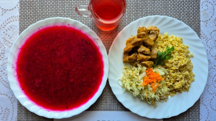 Na zdjęciu znajduję się posiłek w którego skład wchodzi Barszcz ukraiński z ziemniakami, Kasza bulgur, Gulasz wieprzowy, Surówka z kapusty białej z zalewą octową oraz Kompot z jabłek
