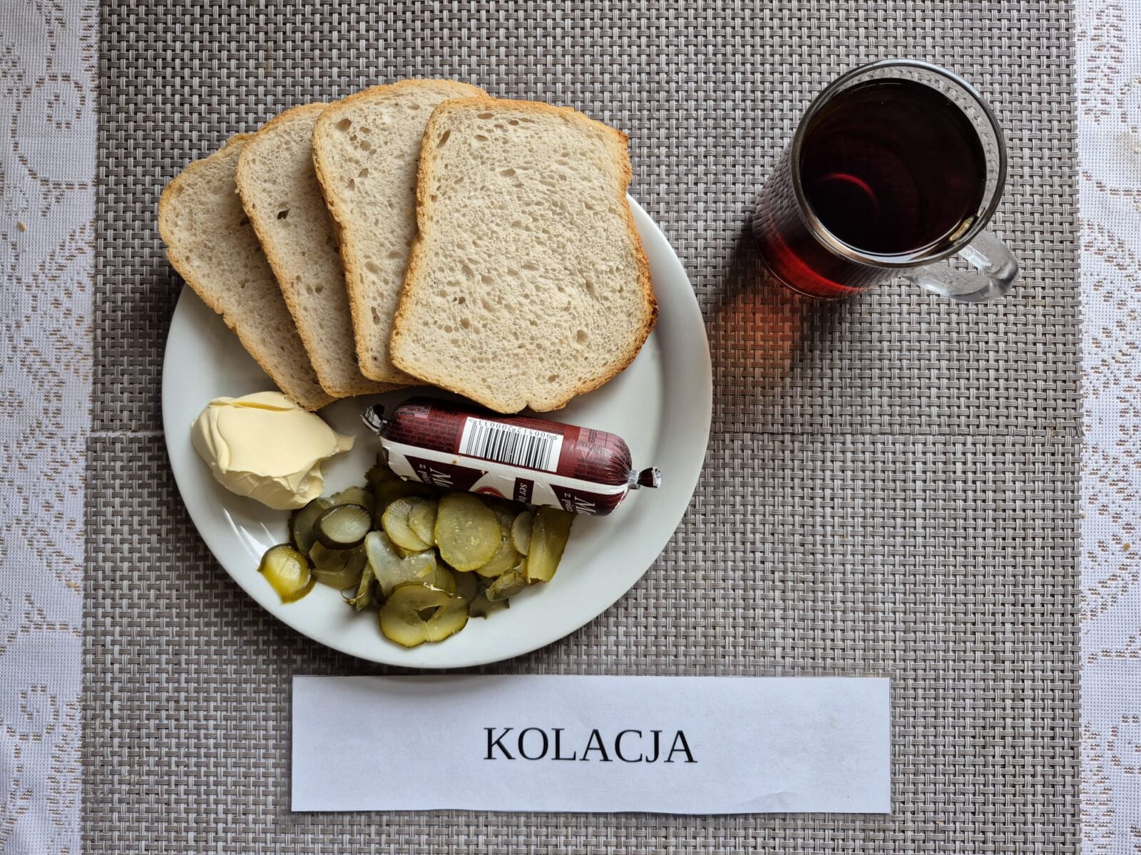 Na zdjęciu znajduję się posiłek w którego skład wchodzi Chleb pszenny, Margaryna Śniadaniowa, Ser topiony, ogórek konserwowy oraz Herbata czarna