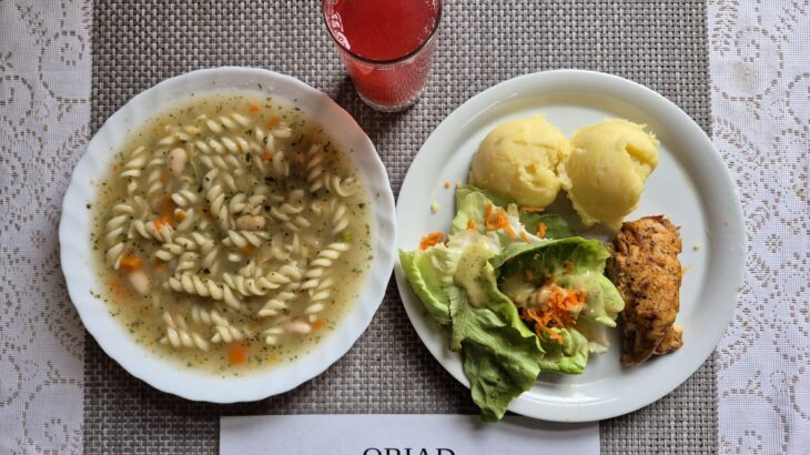 Na zdjęciu znajduję się posiłek w którego skład wchodzi Zupa fasolowa z makaronem, Filet z kurczaka pieczony, Ziemniaki, Sałata masłowa z marchewką oraz Kompot z jabłek