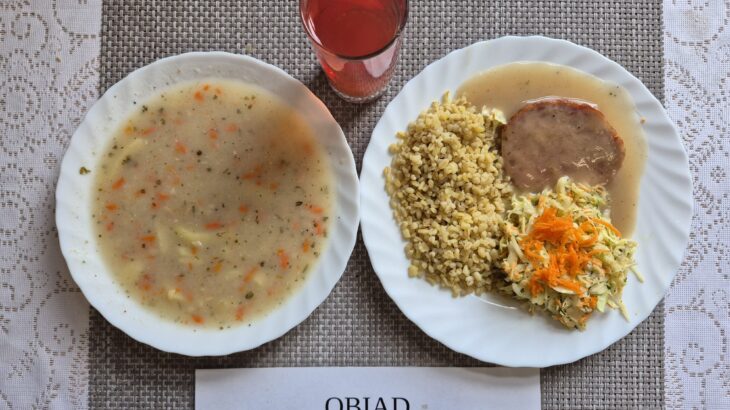 Na zdjęciu znajduję się posiłek w którego skład wchodzi Żurek z ziemniakami, Kasza bulgur, Pieczeń rzymska w sosie własnym, Surówka z kapusty białej oraz Kompot z jabłek