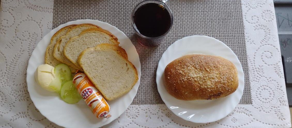 Na zdjęciu znajduję się posiłek w którego skład wchodzi Chleb pszenny, Margaryna Śniadaniowa, Ser topiony, Ogórek zielony oraz Herbata czarna