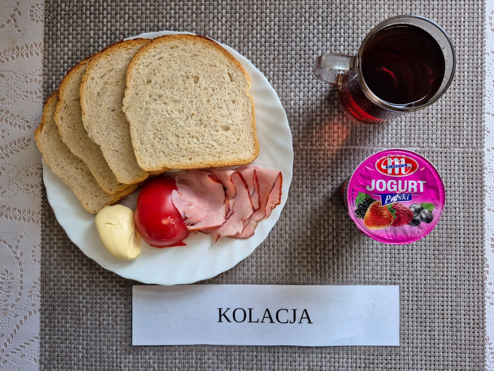 Na zdjęciu znajduję się posiłek w którego skład wchodzi Chleb pszenny, Margaryna śniadaniowa, wędlina wieprzowa, pomidor oraz Herbata czarna