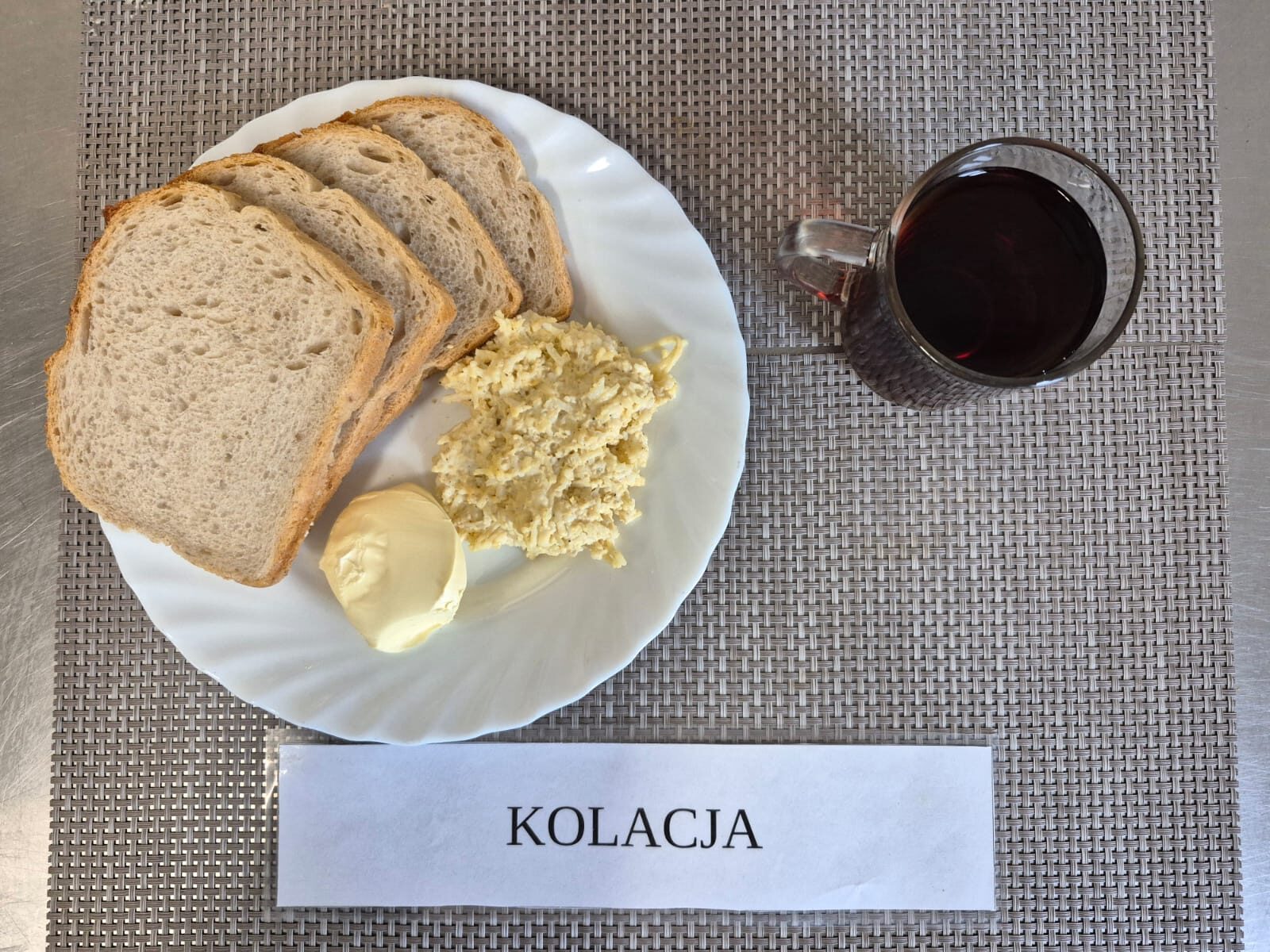 Na zdjęciu znajduję się posiłek w którego skład wchodzi Chleb pszenny, Margaryna Śniadaniowa, Pasta z jajek, sera twardego z dodatkiem czosnku oraz Herbata czarna