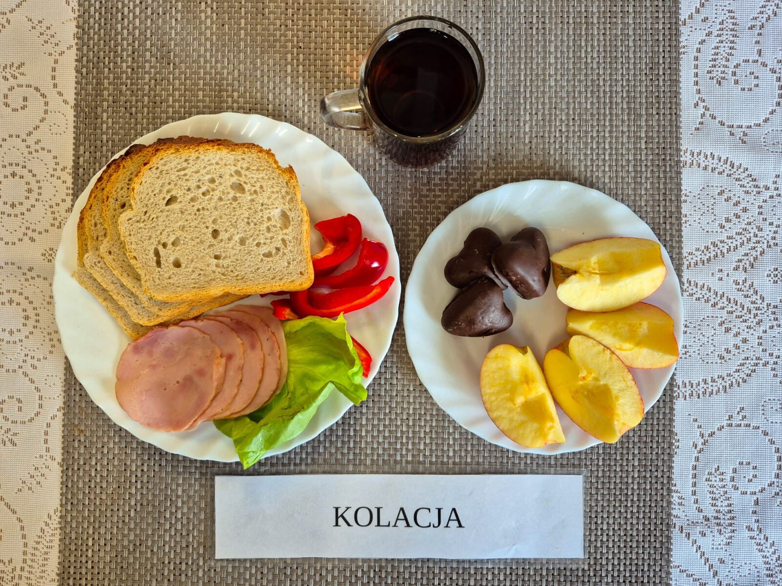 Na zdjęciu znajduję się posiłek w którego skład wchodzi Chleb pszenny, Margaryna Śniadaniowa, Kiełbasa krakowska drobiowa drobiowa, Sałata lodowa, papryka oraz Herbata czarna