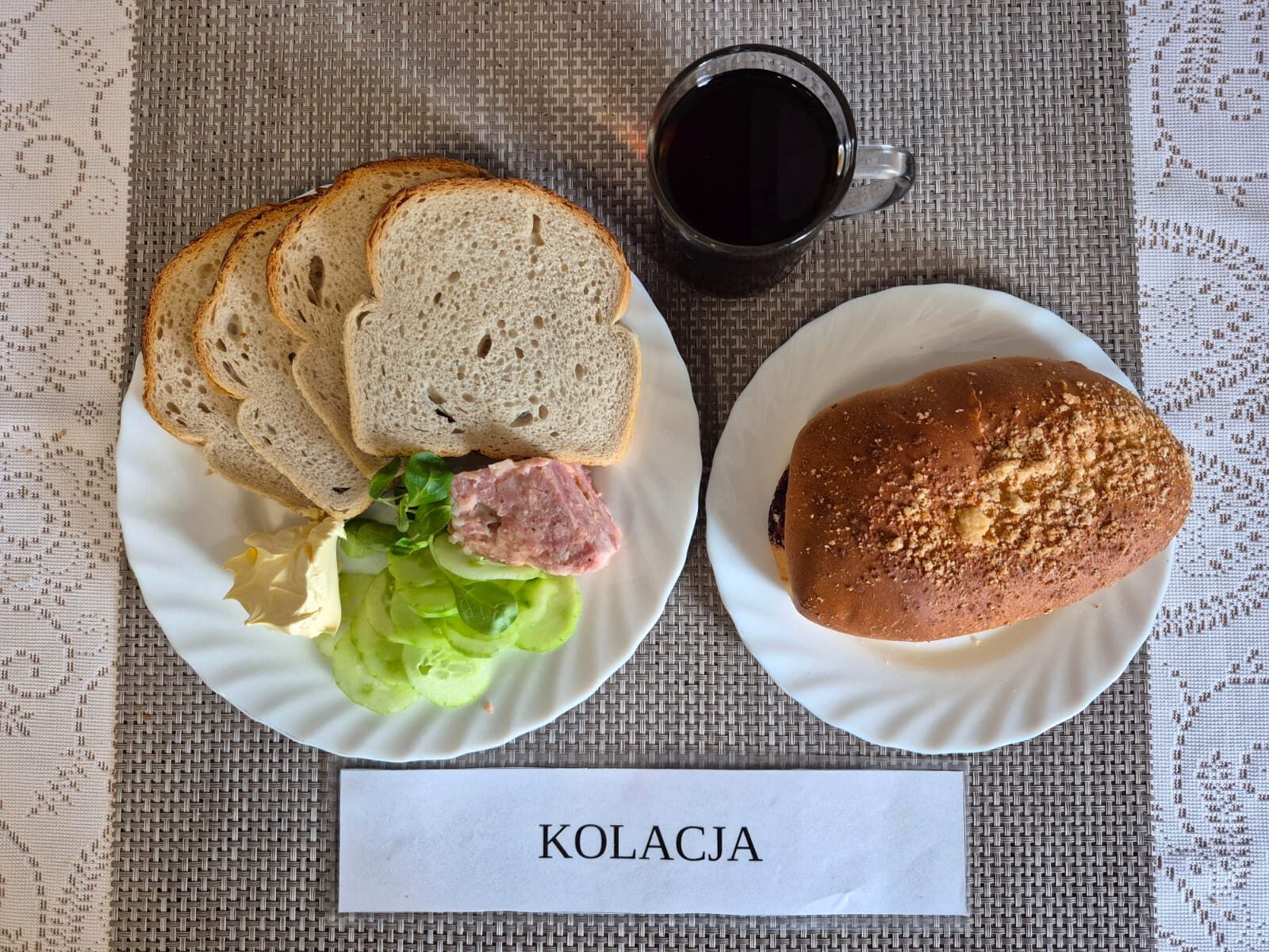 Na zdjęciu znajduję się posiłek w którego skład wchodzi Chleb pszenny, Margaryna Śniadaniowa, konserwa mięsna, Ogórek zielony oraz Herbata czarna