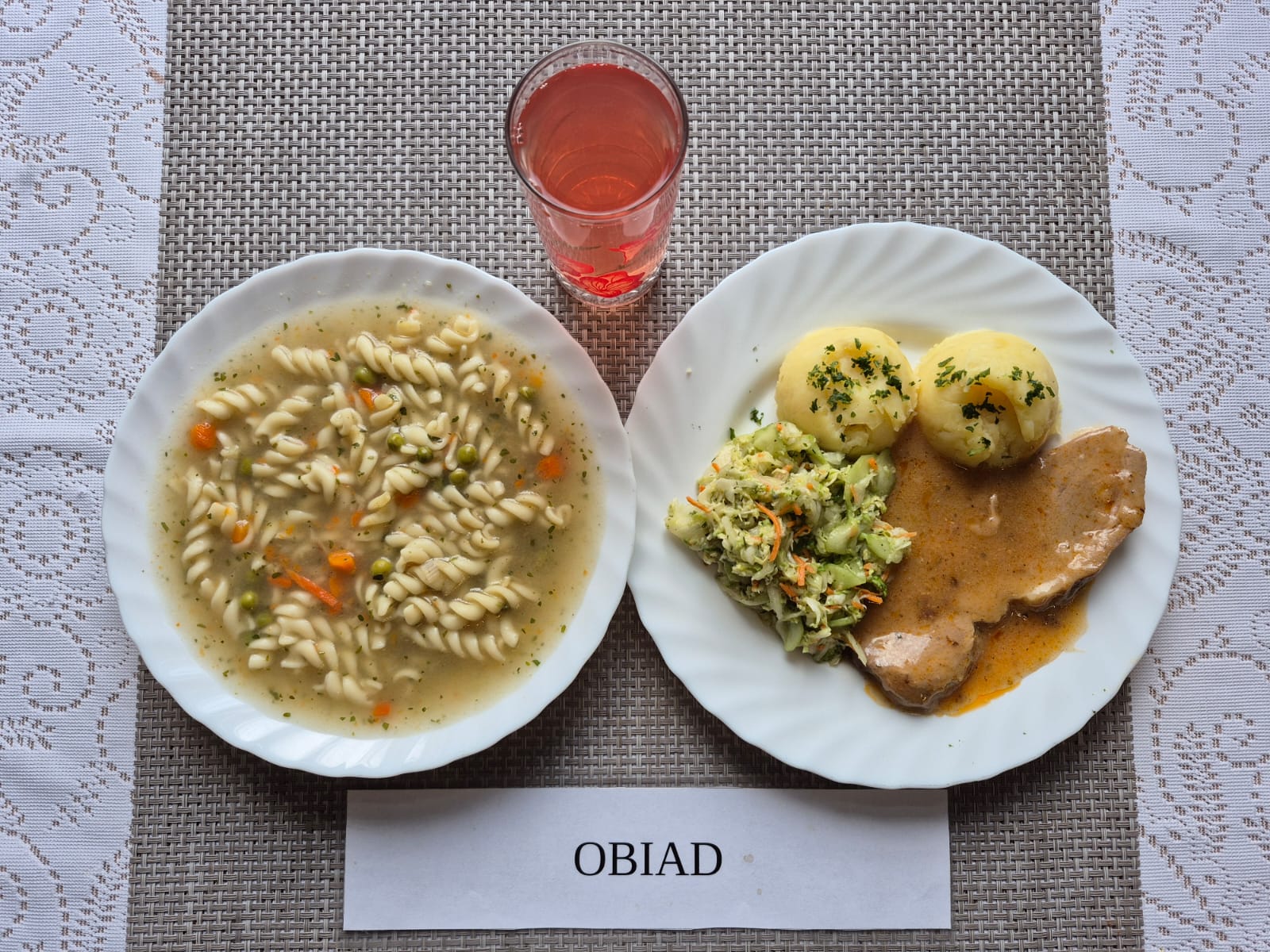 Na zdjęciu znajduję się posiłek w którego skład wchodzi Zupa jarzynowa z groszkiem cukrowym i makaronem 300 ml Ziemniaki 300g karkówka pieczona w sosie własnym 140g Surówka z ogórka zielonego i kapusty pekińskiej i marchewki oraz Kompot z jabłek