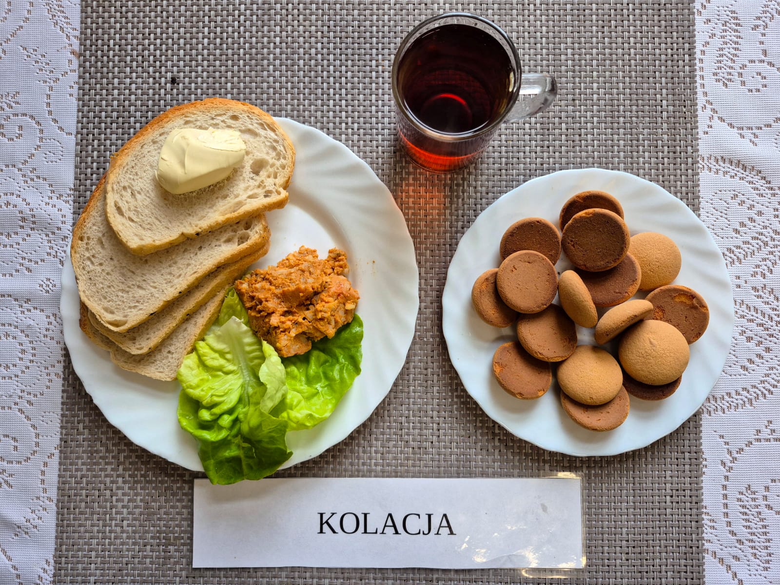 Na zdjęciu znajduję się posiłek w którego skład wchodzi Chleb pszenny, Margaryna Śniadaniowa, Paprykarz szczeciński, Sałata masłowa, ogórek zielony oraz herbata