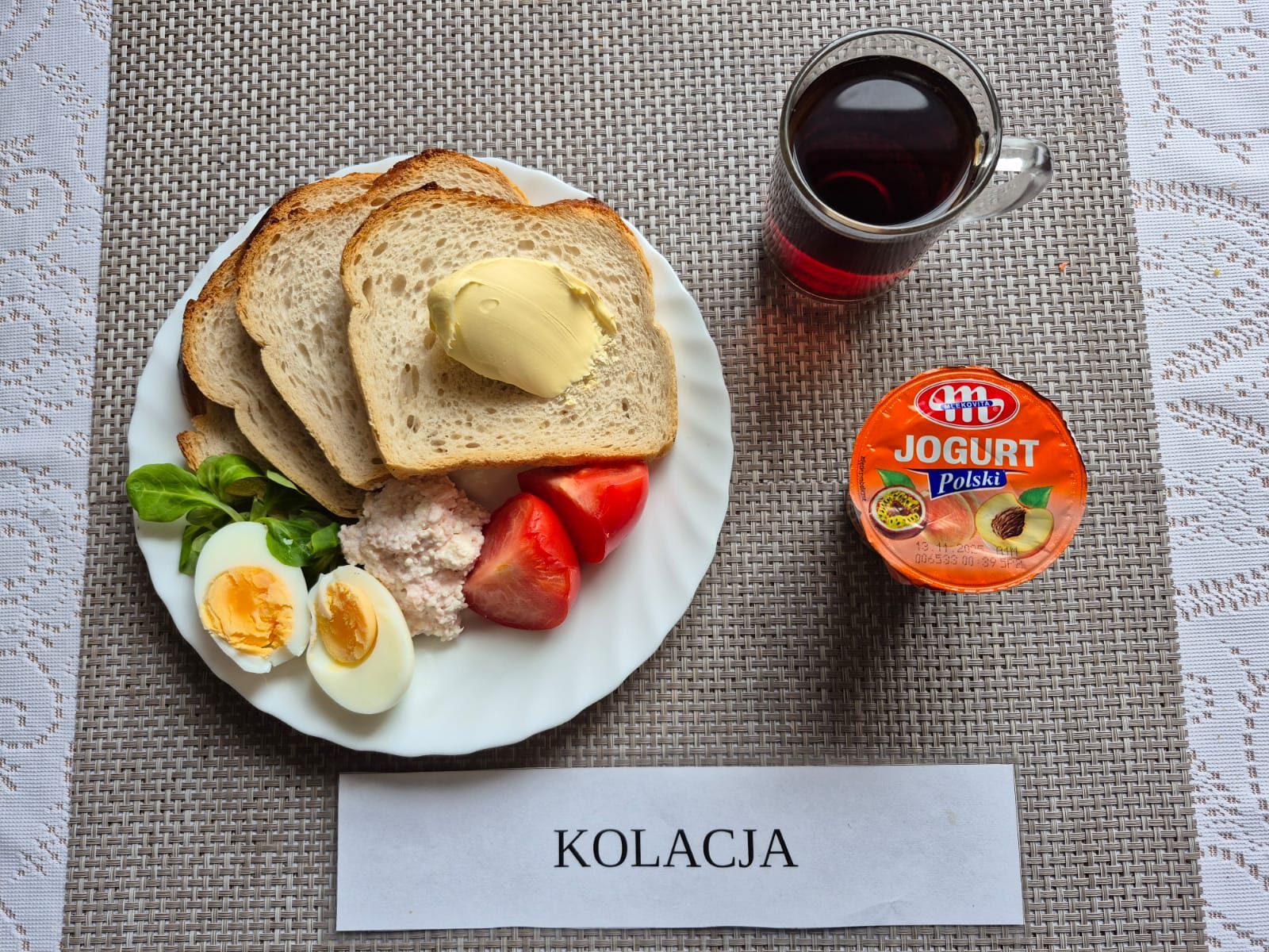 Na zdjęciu znajduję się posiłek w którego skład wchodzi Chleb pszenny, Margaryna śniadaniowa, Twarożek mięsny, jajko 1 szt, pomidor oraz Herbata czarna