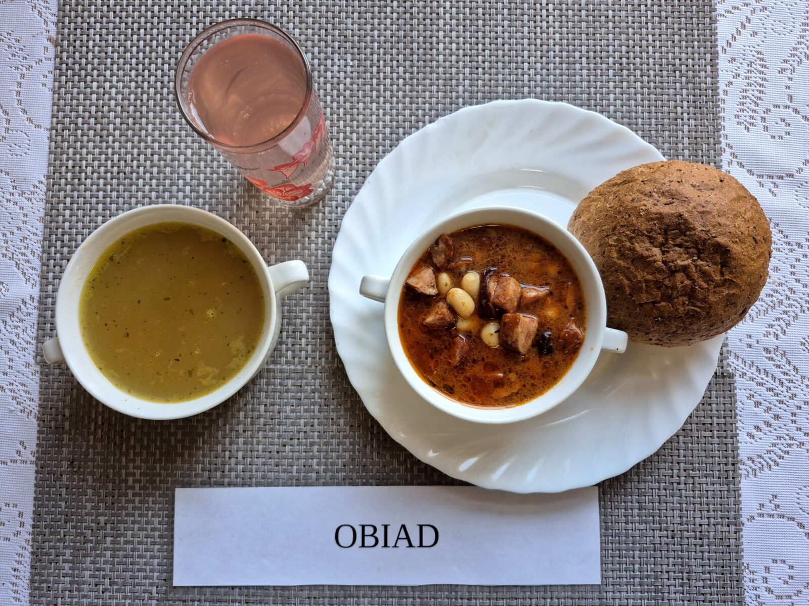 Na zdjęciu znajduję się posiłek w którego skład wchodzi Zupa s soczewicą czerwoną i ziemniakami, Fasolka po bretońsku, Bułka pszenna oraz kompot z jabłek