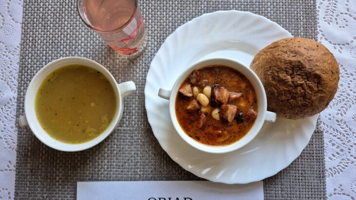 Na zdjęciu znajduję się posiłek w którego skład wchodzi Zupa s soczewicą czerwoną i ziemniakami, Fasolka po bretońsku, Bułka pszenna oraz kompot z jabłek