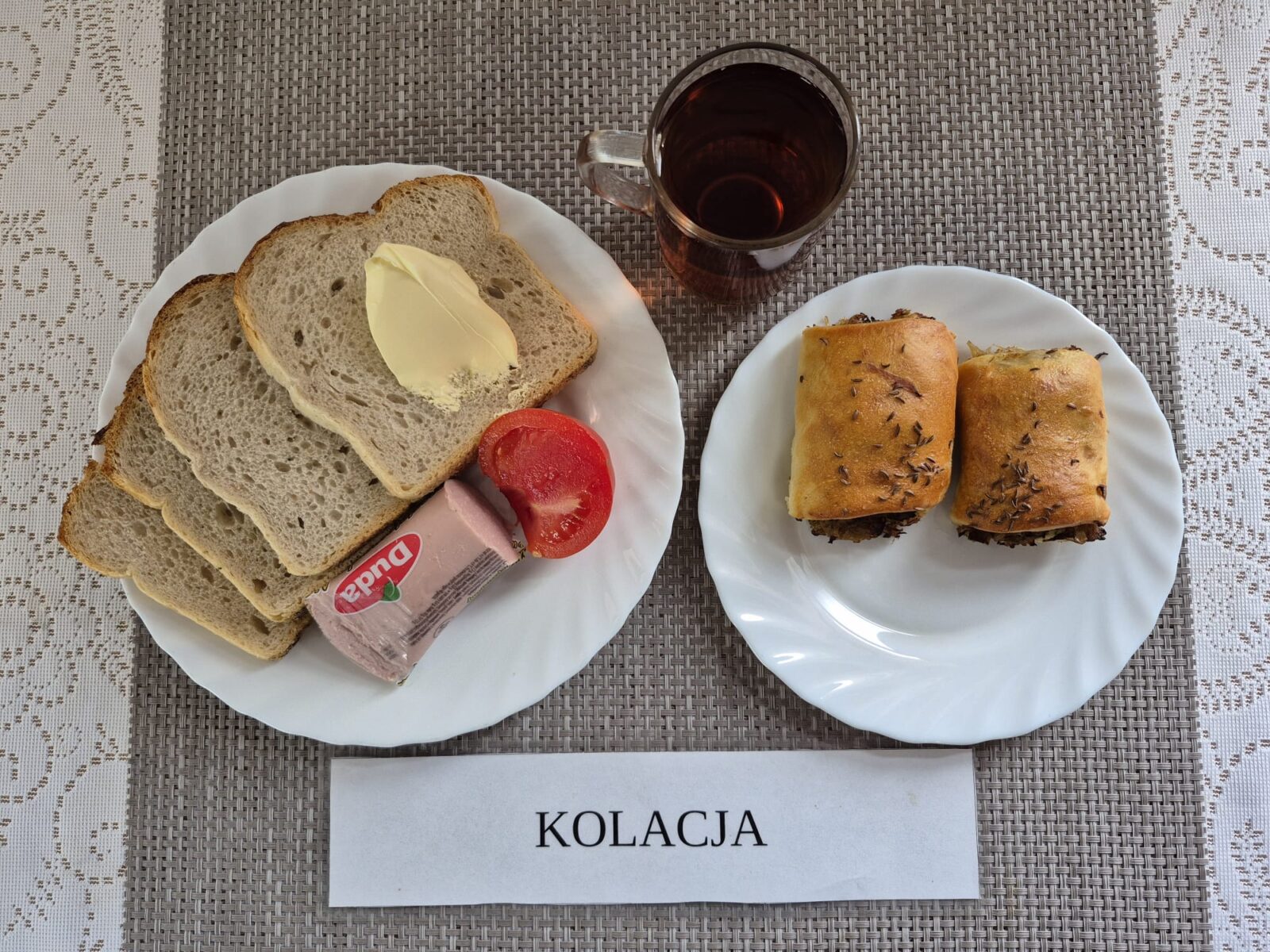 Na zdjęciu znajduję się posiłek w którego skład wchodzi Chleb razowy, Chleb pszenny, Margaryna Śniadaniowa, Pasztet kremowy, Pomidor oraz Herbata czarna