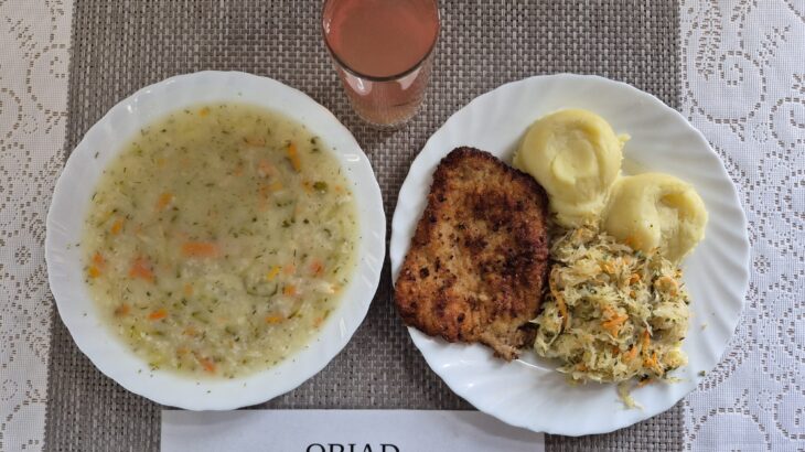 Na zdjęciu znajduję się posiłek w którego skład wchodzi Zupa ogórkowa z ryżem białym, Ziemniaki, Kotlet schabowy, panierwonay smażony, Kapusta kiszona na ciepło oraz Kompot z jabłek
