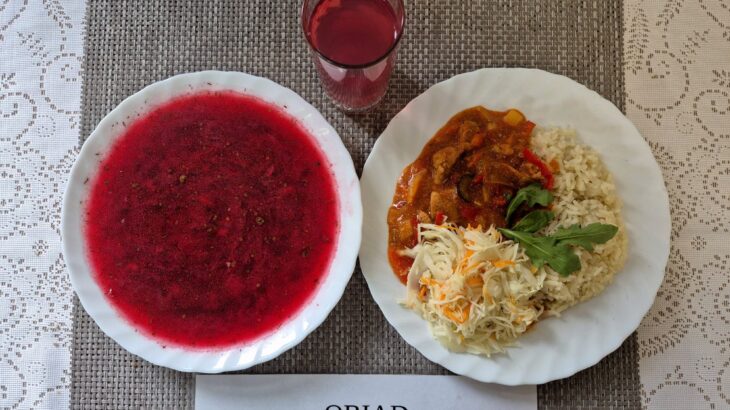 Na zdjęciu znajduję się posiłek w którego skład wchodzi Barszcz ukraiński z fasdolą białą i ziemniakami, Ryż biały, Wieprzowina w sosie słodko-kwaśnym, Surówka z kapusty białej w zalecie octowej, Kompot z jabłek