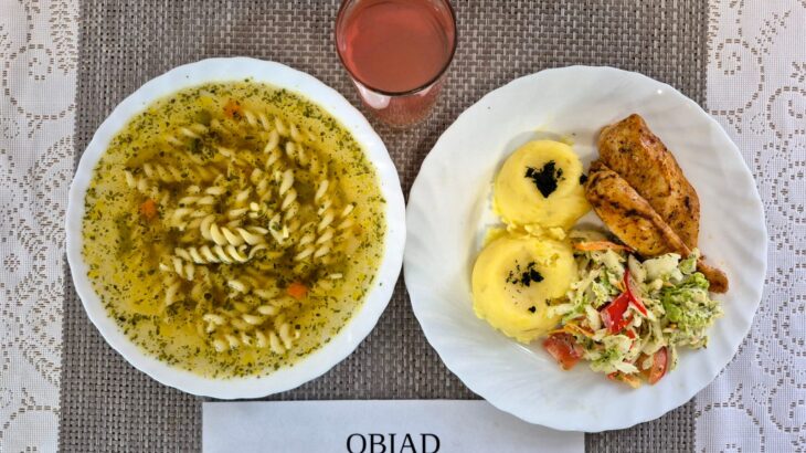 Na zdjęciu znajduję się posiłek w którego skład wchodzi Zupa jarzynowa z makaronem, Ziemniaki, Filet z kurczaka zapiekany w sosie porowym, Surówka z kapusty pekińskiej, marchewki i papryki z sosem majo