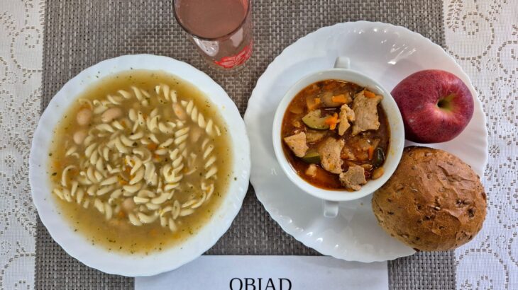 Na zdjęciu znajduję się posiłek w którego skład wchodzi Zupa fasolowa z ziemniakami, Leczo z cukinią, Bułka ziarnista, Jabłko 1 szt oraz Kompot z jabłek