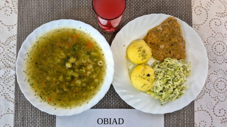 Na zdjęciu znajduję się posiłek w którego skład wchodzi Zupa brokułowa z makaronem, Ziemniaki, Bitka wieprzowa w sosie własnym, Surówka z kapusty pekińskiej i ogórka zielonego oraz Kompot z jabłek