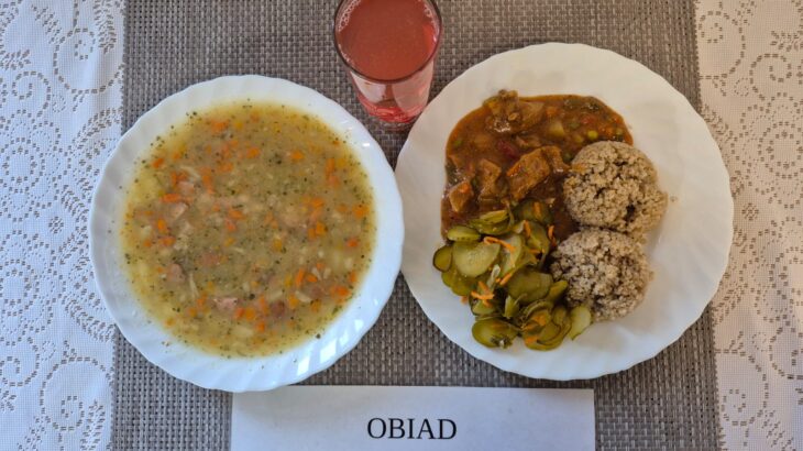 Na zdjęciu znajduję się posiłek w którego skład wchodzi Zupa grochowa z ziemniakami i kiełbasą, kasza jęczmienna, gulasz wieprzowy, surówka z ogórka kiszonego oraz Kompot z jabłek