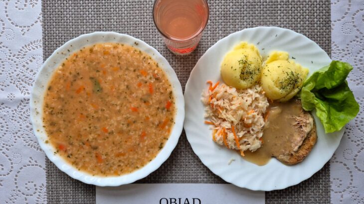 Na zdjęciu znajduję się posiłek w którego skład wchodzi Zupa pomidorowa z ryżem białym, Ziemniaki, Schab pieczony w sosie własnym, Surówka z marchewki oraz kompot