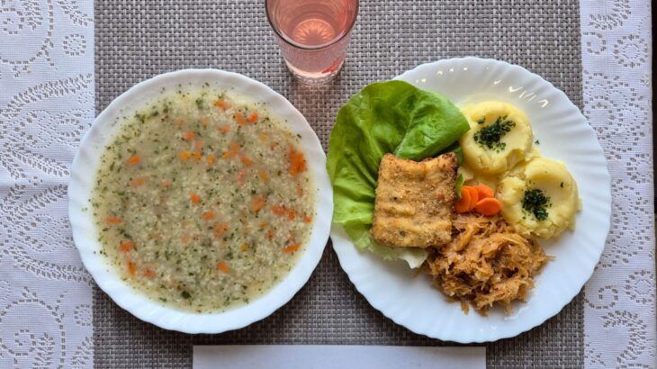 Na zdjęciu znajduję się posiłek w którego skład wchodzi Zupa ryżowa, Ryba smażona, Ziemniaki, Surówka z kapusty kiszonej oraz kompot z jabłek