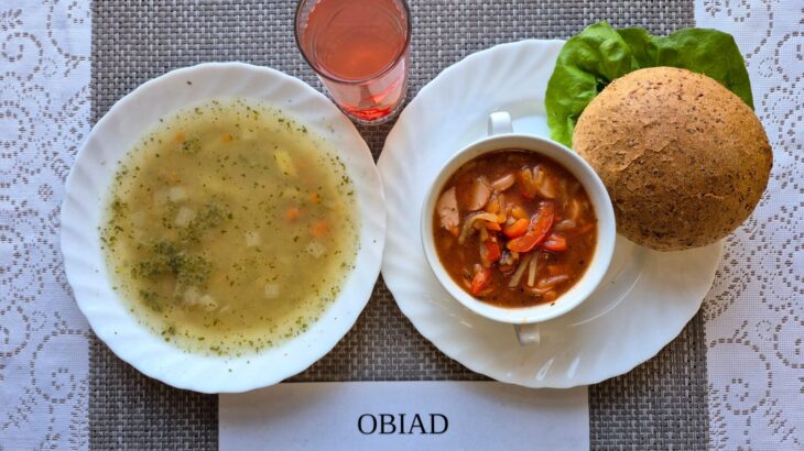 Na zdjęciu znajduję się posiłek w którego skład wchodzi Zupa ziemniaczana z czosnkiem, Leczo z parówką wieprzową, Bułka grahamka, gruszka oraz Kompot z jabłek