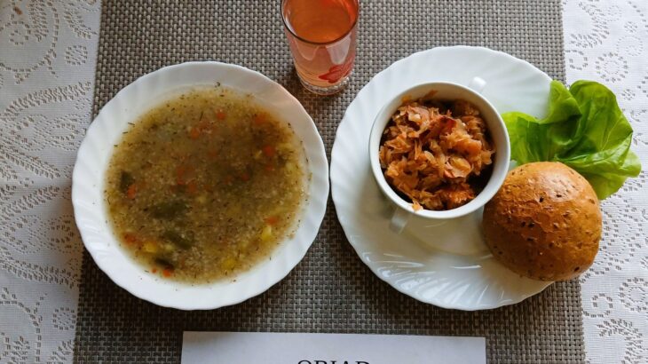 Na zdjęciu znajduję się posiłek w którego skład wchodzi Zupa krupnik ziemniakami, Bigos z wędliną wieprzową, Bułka wieloziarnista, kompot z jabłek